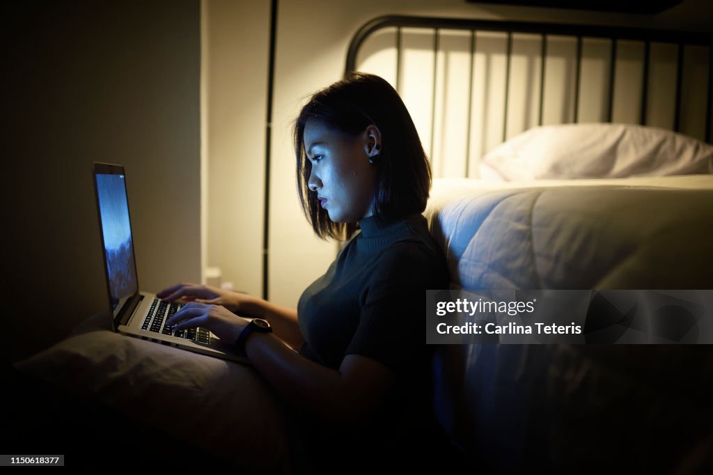 Woman working on her laptop in her bedroom at night