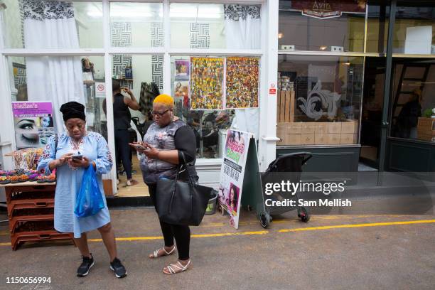 Two women outside a hairdressers using their mobile phones at Brixton Village on the 23rd May 2019 in London in the United Kingdom.