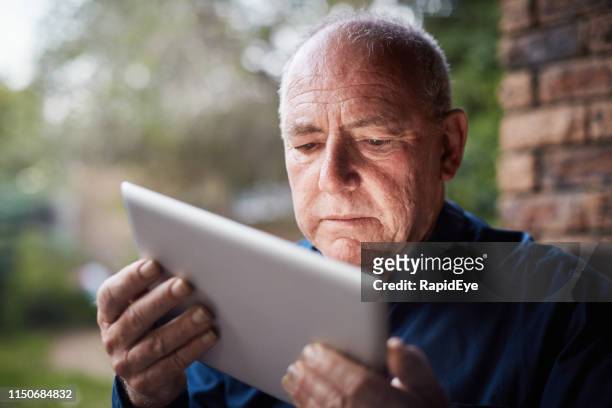 el hombre mayor que usa la tableta digital parece confundido, frunciendo el ceño - entrecerrar los ojos fotografías e imágenes de stock