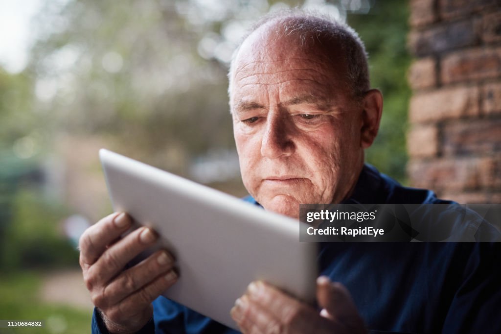 Senior man met behulp van digitale Tablet lijkt verward, fronsen