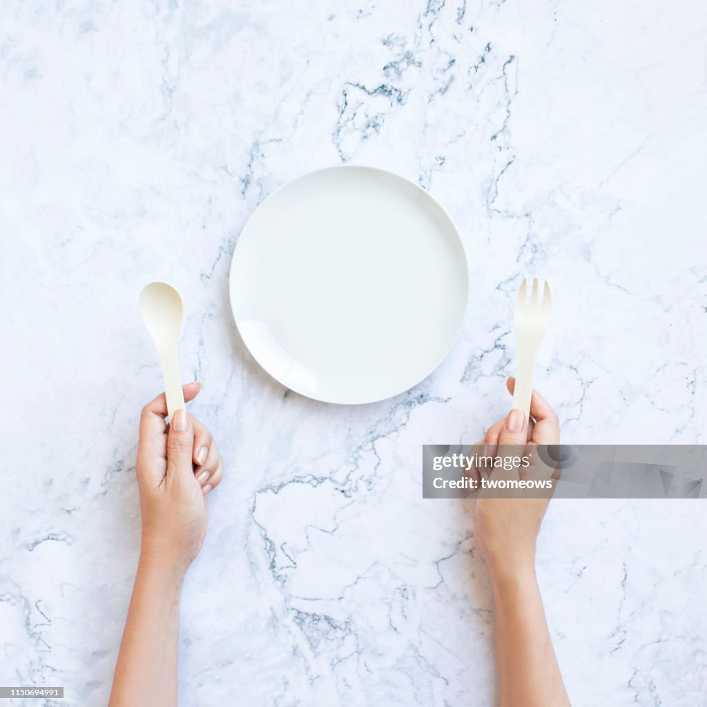 Hand ready to eat and empty plate on marble table top.