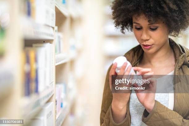 woman reading label of medicine bottle - pharmacy customer stock pictures, royalty-free photos & images