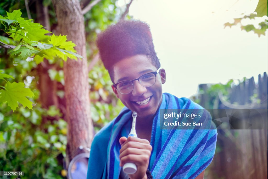 Teenage boy with afro flat top hairstyle holding electric toothbrush in garden, portrait
