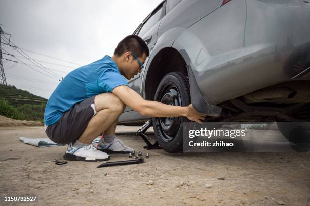 a young man changing a tire on the side of the road - spare tyre stock pictures, royalty-free photos & images