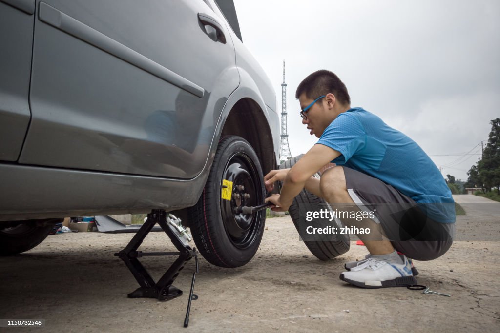 A young man changing a tire on the side of the road