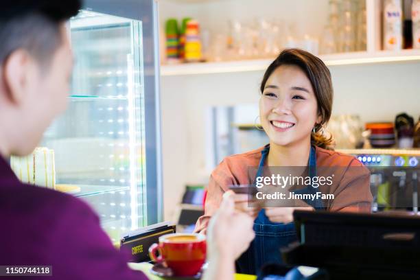 beautiful asian waitress receiving credit card payment from customer in café. - quick cafe stock pictures, royalty-free photos & images