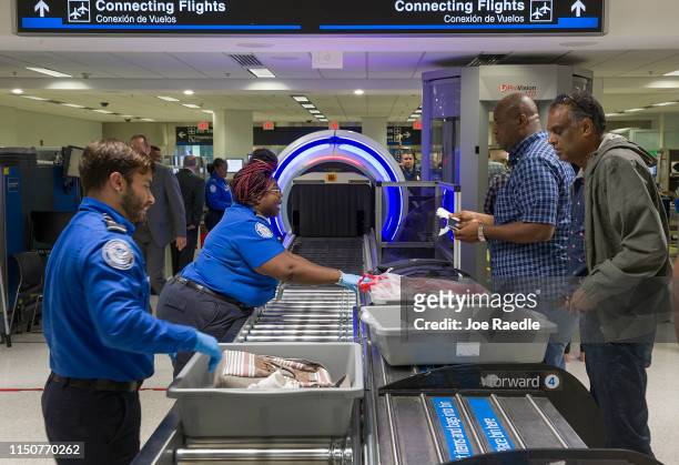 Transportation Security Administration agents help travelers place their bags through the 3-D scanner at the Miami International Airport on May 21,...