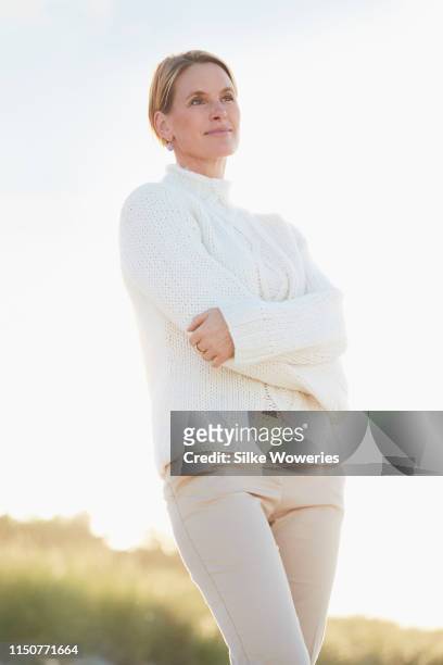 portrait of a mature adult woman standing in front of sand dunes looking afar - three quarter length stock pictures, royalty-free photos & images