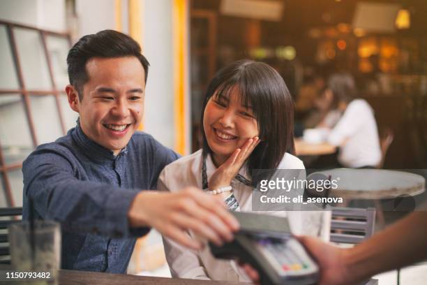 asian young couple paying by smart phone in restaurant - paying for dinner imagens e fotografias de stock