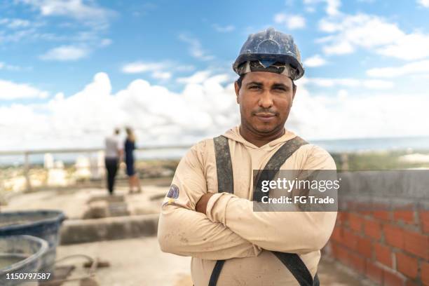 bauarbeiter steht mit in einer baustelle gekreuzten arme - hispanic construction worker stock-fotos und bilder