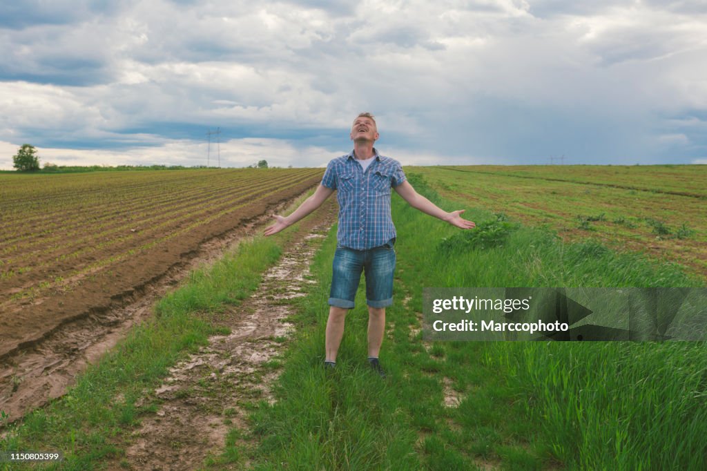 Adult farmer at his corn crop seedling muddy agricultural field just after storm shower in springtime praise the Lord for the rain.