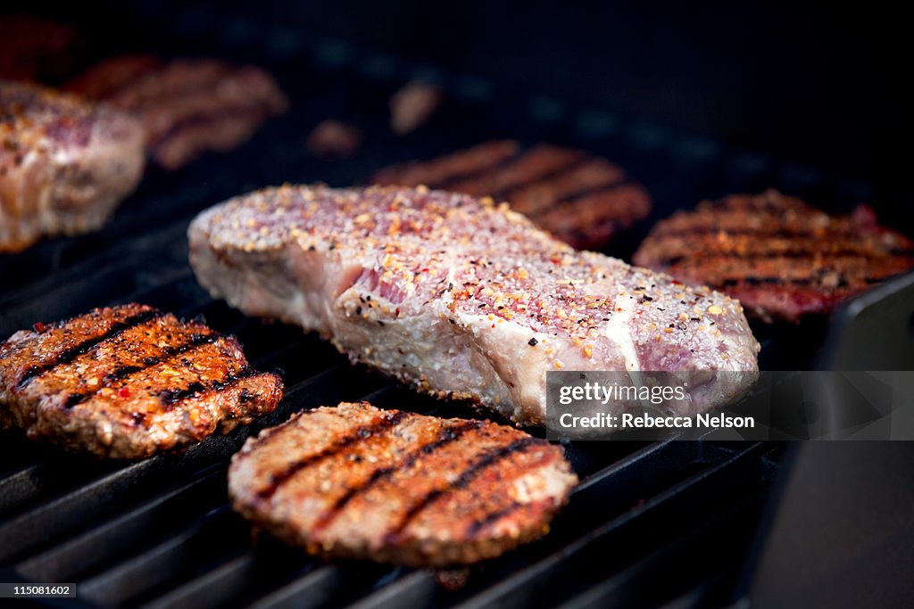 Hamburgers and strip steaks cooking on gas grill