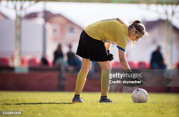 female goalkeeper adjusting a ball on grass at stadium. - woman goalie stock pictures, royalty-free photos & images