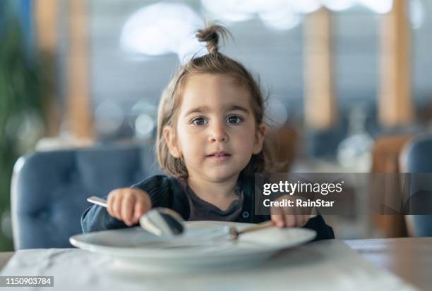 bambina che tiene forchetta e cucchiaio con - hungry foto e immagini stock