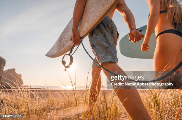 side view of surfing couple. - surfer by the beach australia stock-fotos und bilder
