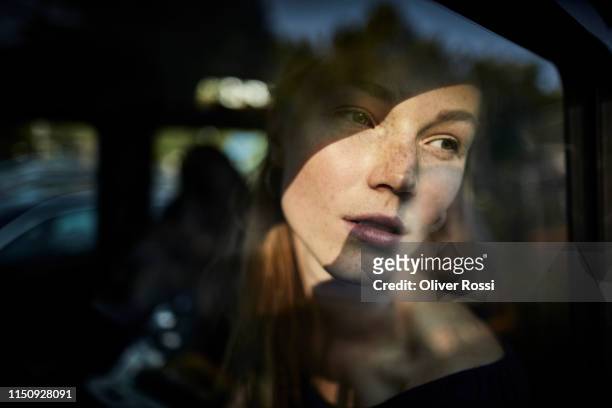 pensive young woman looking out of car window - reflection stock-fotos und bilder