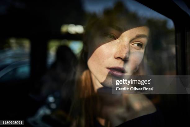 pensive young woman looking out of car window - woman looking out window stockfoto's en -beelden