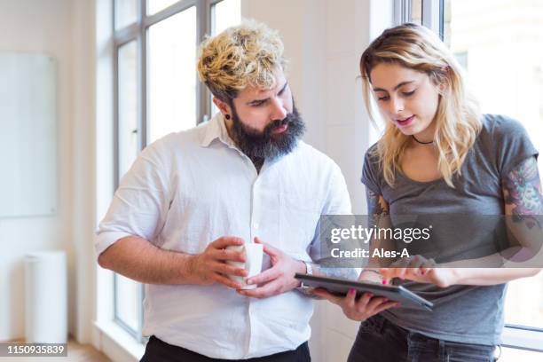 two young colleagues using a digital tablet - tattoo man and woman stock pictures, royalty-free photos & images