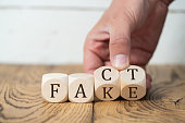 hand is turning two of four cubes, changing the word FACT to FAKE