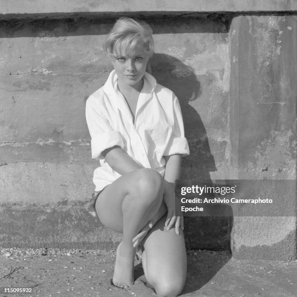 Italian actress Virna Lisi, wearing a white shirt, and hotpants, standing on her knees, leaning against the wall, on the beach, Lido, Venice 1958.
