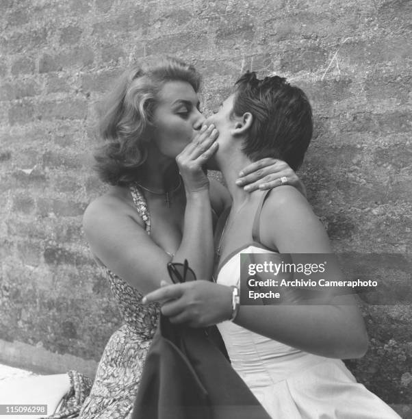 Italian actress Sophia Loren, wearing a floral dress, kissing on the lips her sister Maria Scicolone holding sunglasses and a blazer, Venezia 1955.