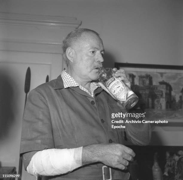 American writer Ernest Hemingway, wearing a short sleeves shirt over a plaid shirt, his hurted arm bendaged, drinking vodka from the bottle, Venice...