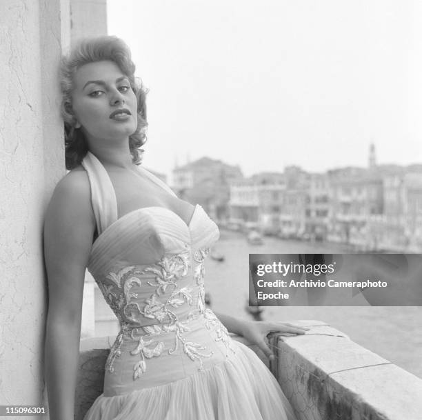 Italian actress Sophia Loren leaning on a wall, portayed on a terrace on the Canal Grande, wearing a white embroidered dress, Venice, 1955.