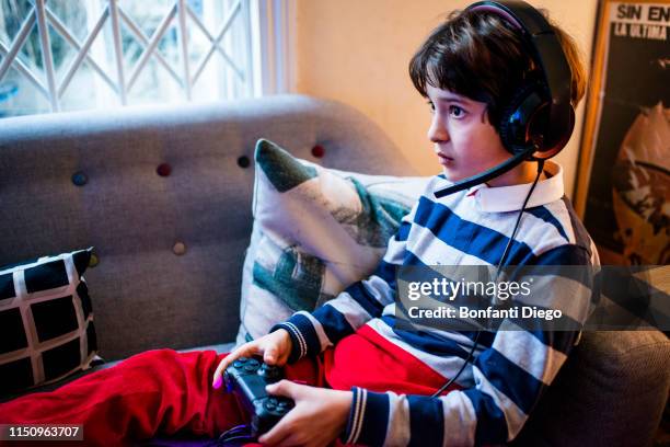 boy sitting on sofa wearing headset and  using game controller - pre game stockfoto's en -beelden