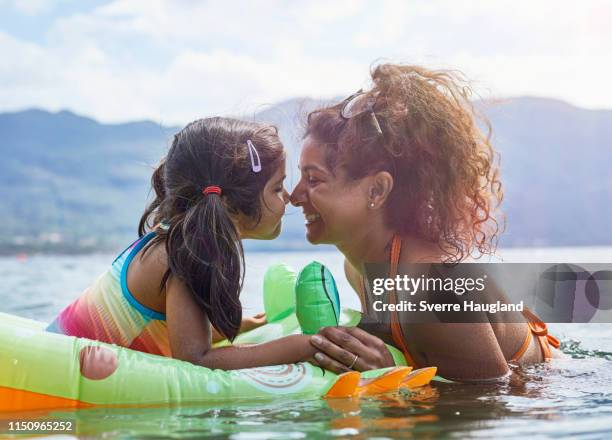 mother rubbing noses with daughter on inflatable frog in lake - indian mother and child stock pictures, royalty-free photos & images