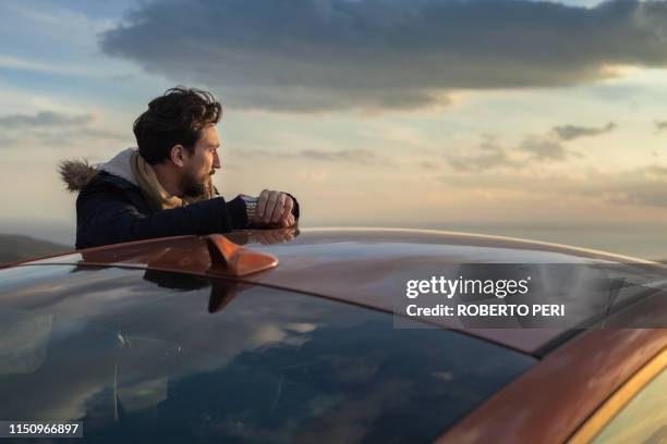 man resting against car on roadside, enjoying view on hilltop - effet miroir homme photos et images de collection