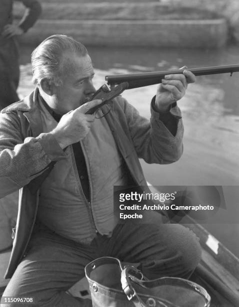 American writer Ernest Hemingway sitting on a boat, hunting ducks in a pond in Torcello, checking the bullet through the barrel of the rifle, Venice...