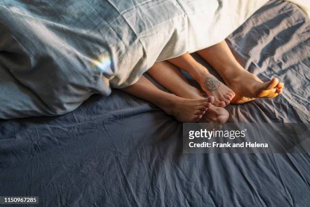 couple's feet sticking out from under duvet in bed - man feet stockfoto's en -beelden
