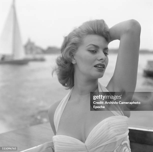 Italian actress Sophia Loren, wearing a white embroidered dress, posing for the photographer, a sail on the sea in the background Venice, 1955.