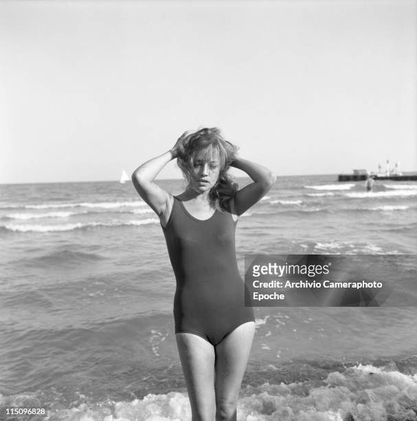 French actress Jeanne Moreau, wearing a swimming suit, holding her hair, standing on the seashore, feet in the water, Lido, Venice 1961.