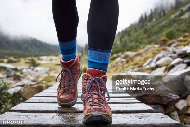 female hiker hiking across wooden footbridge, cropped view of legs and hiking boots - hiking shoes stock-fotos und bilder