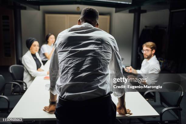 businessman in front of team at conference table meeting, rear view - masculinity stock pictures, royalty-free photos & images