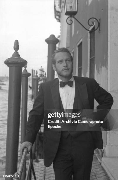 American actor Paul Newman, wearing a tuxedo and a bow tie, a pack of Red Marlboro cigarettes in his pocket, a hand on the hip, some hooden poles...