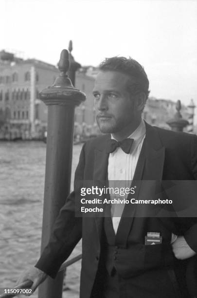 American actor Paul Newman, wearing a tuxedo and a bow tie, a pack of Red Marlboro cigarettes in his pocket, some hooden poles behind him and the...