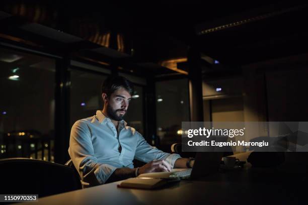 mid adult businessman in office at night typing on laptop - working late foto e immagini stock