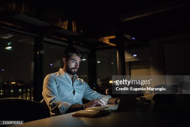 mid adult businessman in office at night typing on laptop - working late stock pictures, royalty-free photos & images