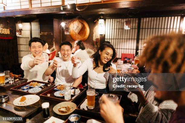 group of mixed-raced travelers enjoying drinking alcohol in japanese style pub - tokyo food stock pictures, royalty-free photos & images