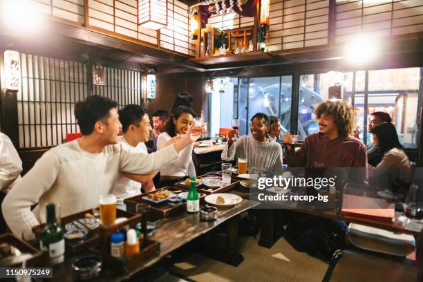 group of mixed-raced travelers enjoying drinking alcohol in japanese style pub - izakaya stock pictures, royalty-free photos & images