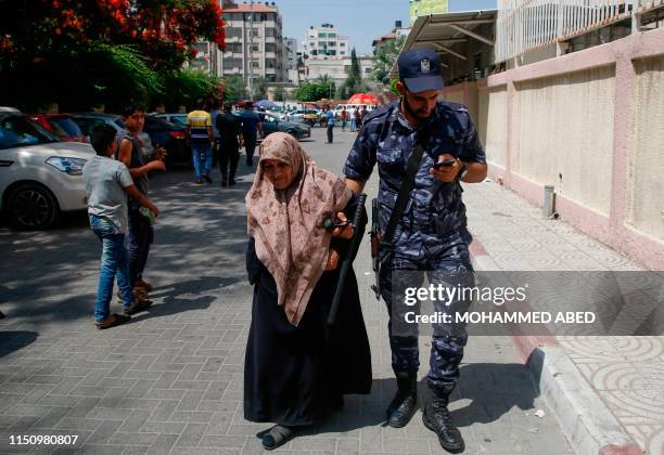 Member of the Palestinian security forces helps an old lady outside the post office, in Gaza City on June 20, 2019. - Qatar distributed $100 grants...