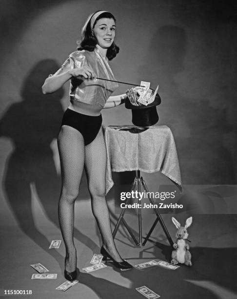 Woman pointing to dollar bills, with a stuffed rabbit on the floor, during a magic trick circa 1960.