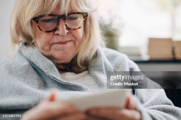 retired senior woman wrapped in blanket reading e-book in room at home - wrapped in a blanket stock pictures, royalty-free photos & images