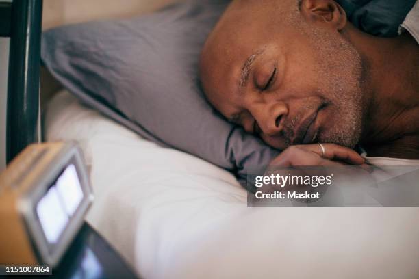 retired senior man sleeping on bed by alarm clock at home - black man sleeping in bed stock-fotos und bilder