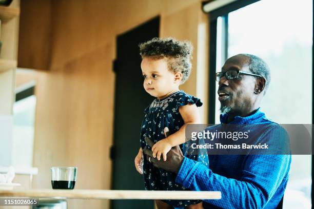 Grandfather holding toddler granddaughter while sitting at dining room table