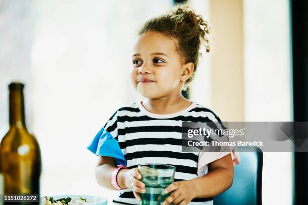 young girl holding water glass while dining at kitchen table - african girl drinking water stock-fotos und bilder