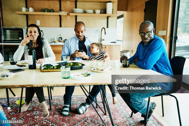 young girl looking at fathers smart phone during multigenerational family meal - sitting at table looking at camera stock-fotos und bilder