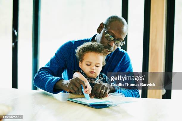 Grandfather helping granddaughter color at dining room table